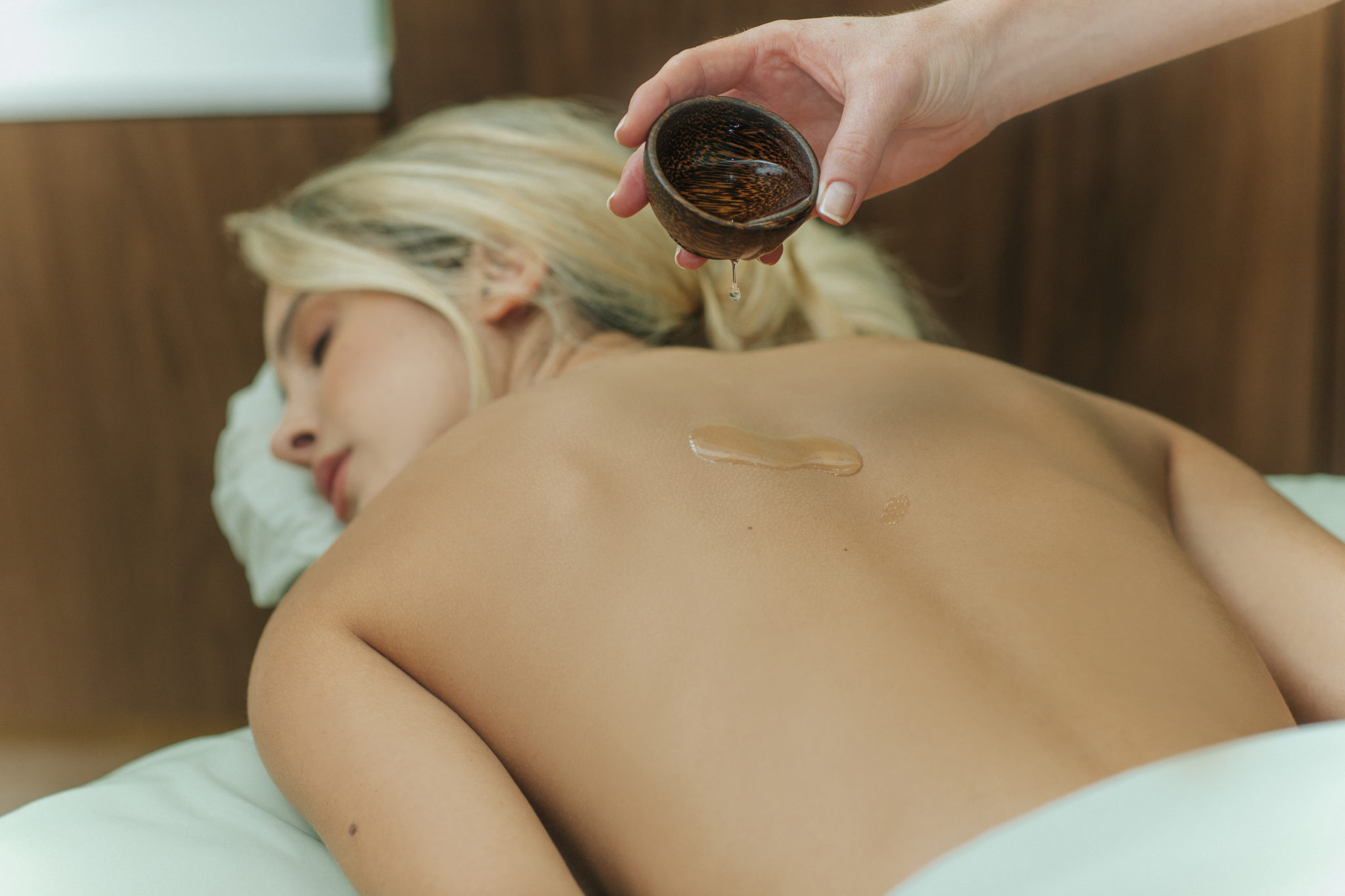 hand of a masseur dropping essential oil to a woman's back