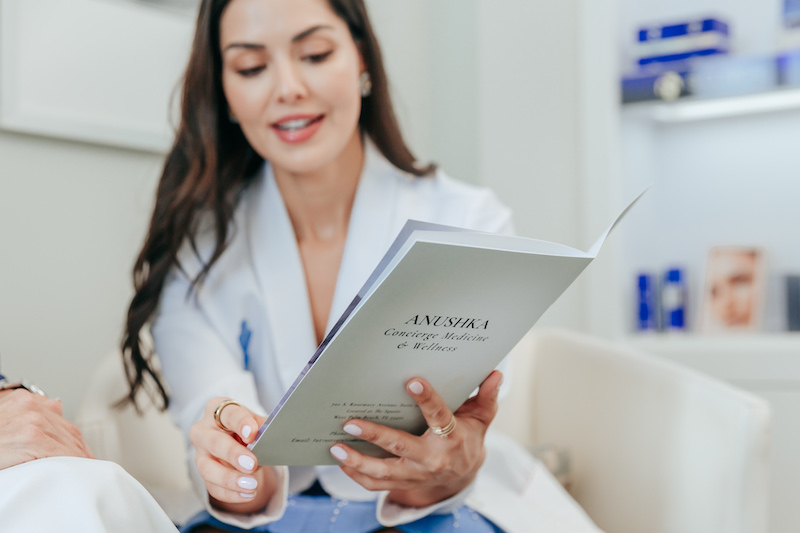 An Anushka provider sitting in a treatment room with a pamphlet explaining to a client the benefits of Morpheus8 in West Palm Beach