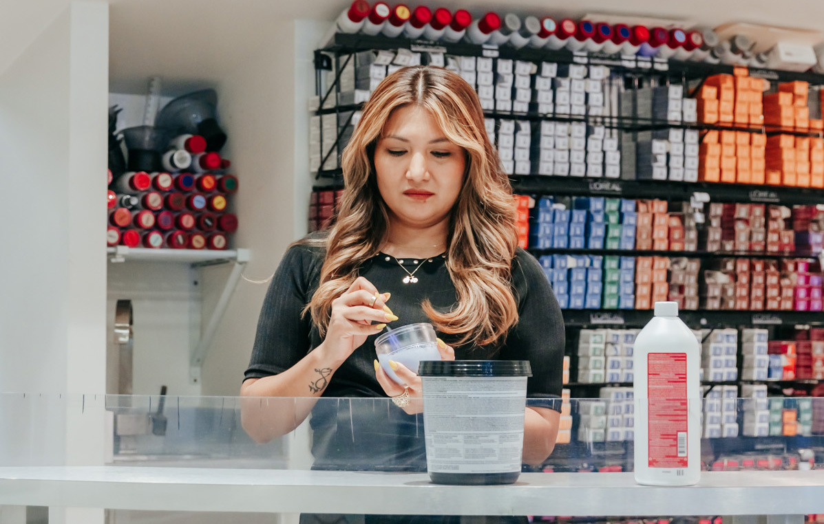 Cropped photo showing Anushka hair color specialist with many color boxes behind her at a counter mixing a new hue of hair color near me in Palm Beach.